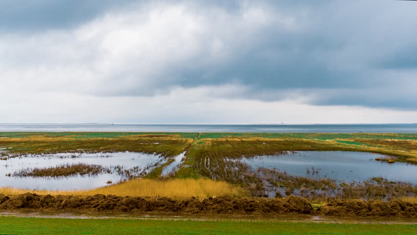 Timelapse scene of tranquil wetlands and marshes with reflections under cloudy skies near the East Frisian Islands, Lower Saxony, Germany. Rain clouds move peacefully over the wetlands.