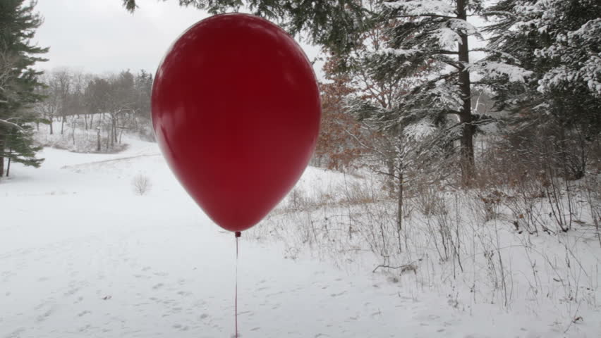 Red helium balloon in a snow landscape with evergreen trees in background.