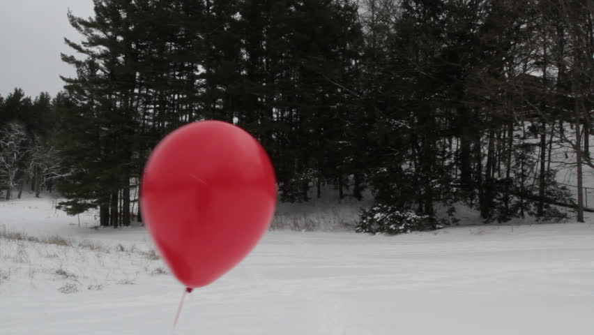Red helium balloon escapes in a snow landscape with evergreen trees in