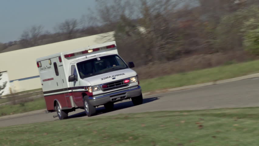 Ambulance driving on empty country road with lights flashing in daytime. Canted