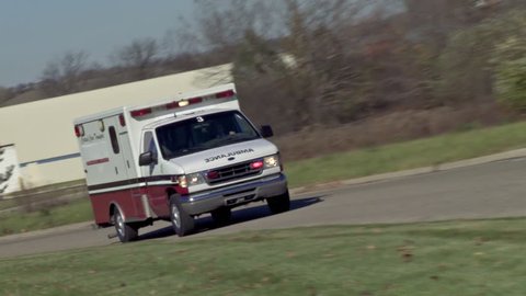 Ambulance driving on empty country road with lights flashing in daytime. Canted camera angle.