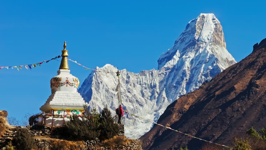 Mountain climber raising colorful prayer flags on wooden stupa, Ama Dablam mountain towering behind in Everest Region, Nepal