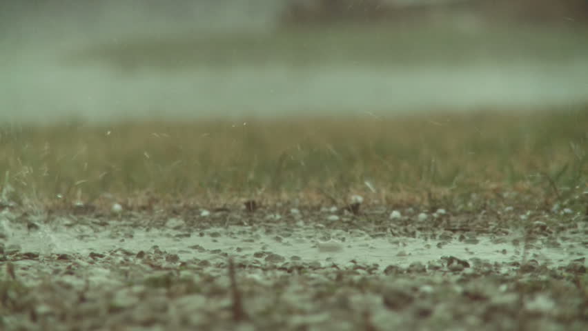 Big drops of rain hitting the ground and splashing during a storm. Recorded in