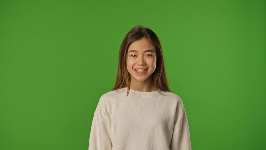 Asian girl child looks around and saying wow with amazed face at camera, positive expression, isolated on chroma key green screen studio background mockup.