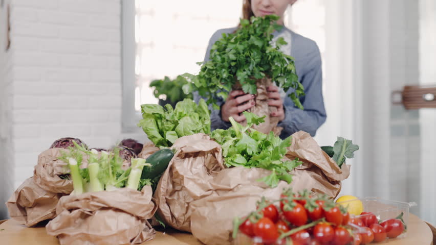 Woman holding a bunch of fresh parsley and lettuce wrapped in eco paper bags from farmers market, fresh organic fruits and vegetables for balanced diet. High quality 4k footage