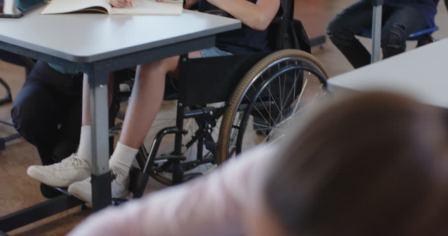 In school, teacher assisting student in wheelchair with writing in classroom. Education, inclusivity, support, teaching, disability, learning