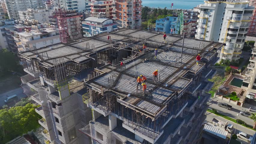 Aerial Video of a Construction Crew Working on Roofing, Concrete Pouring, and Installing Metal Beams