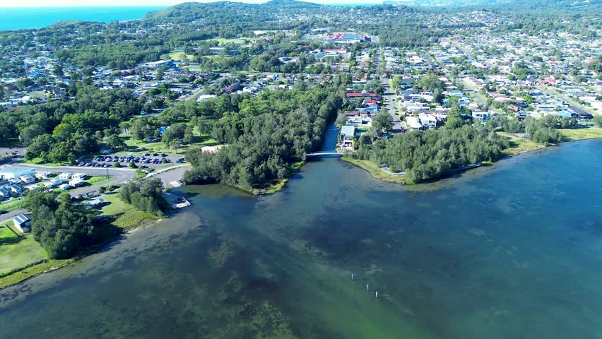 Drone aerial landscape of pathway bridge over lake creek water inlet surrounded by rural town housing, trees and public carpark Long Jetty Killarney Vale Central Coast Australia travel tourism nature