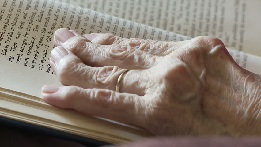 Elderly woman's hands, deformed by arthritis, turn the pages of an old book. 