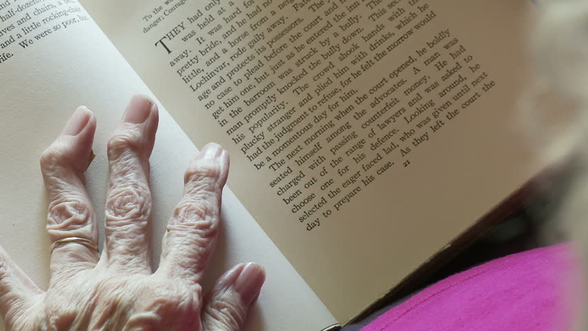 Elderly woman's hands, deformed by arthritis, turn the pages of an old book. 