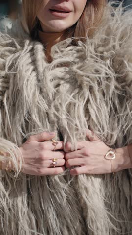 A woman gracefully slides her hands down a shaggy, textured fur coat, adorned with elegant gold jewelry, including rings and a bracelet, highlighting a chic and luxurious aesthetic - vertical, slowmo