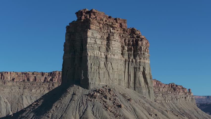 A low-flying, slowly rotating drone shot, angled up at a towering rock pillar known as Chimney Rock, or Jackson Butte, one of three in the Mesa Verde Region, located in southwestern corner of Colorado