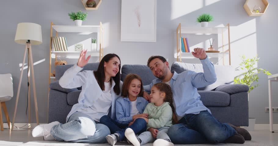 Happy young smiling parents mother, father with children sitting on floor at home making house roof by hands above. Insurance, care,love and family protection concept. 4k video. Slow motion video.
