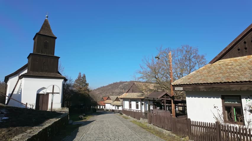 Street view from the Old Town of Holloko with a church and traditional paloc style of houses on a sunny day in Hungary.