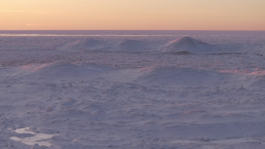Frozen Lake Huron with snow-covered hills under the soft glow of sunset light