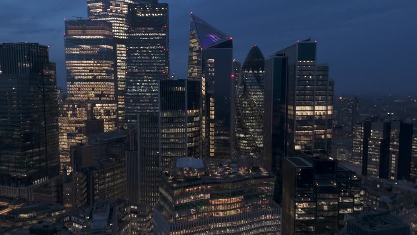 Aerial orbital view of central London cityscape at night showcasing a vibrant cluster of illuminated high-rise glass towers and neon-lit spires