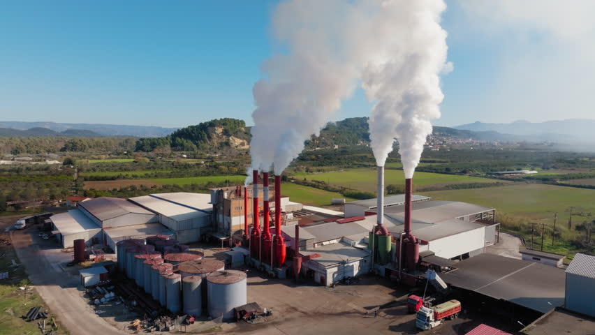 Industrial smokestacks billowing smoke at Olive Pomace refined oil factory causing air and odour pollution surrounding natural landscape, Aerial view