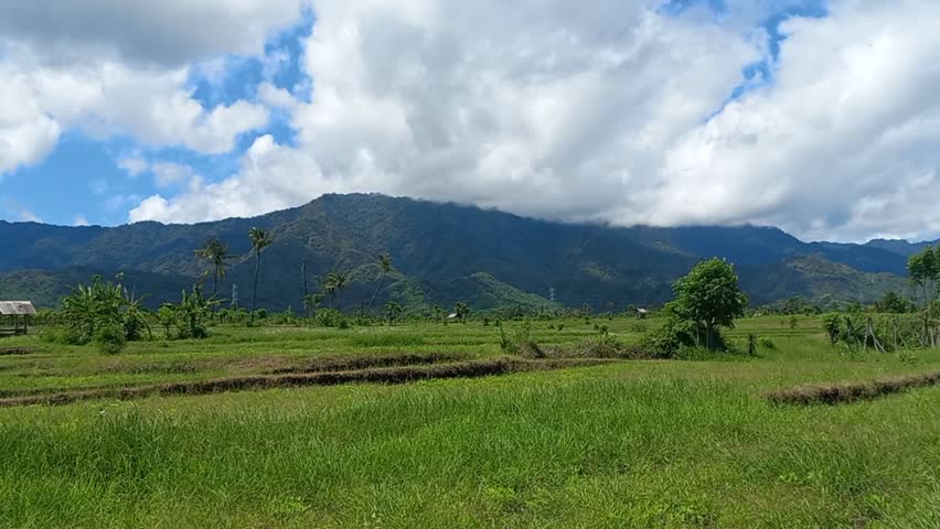 View of a stretch of grass with a backdrop of high hills and blue sky and white clouds in the countryside