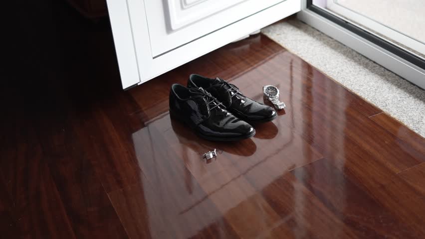 Glossy black wedding shoes with cufflinks and a watch on a wooden floor