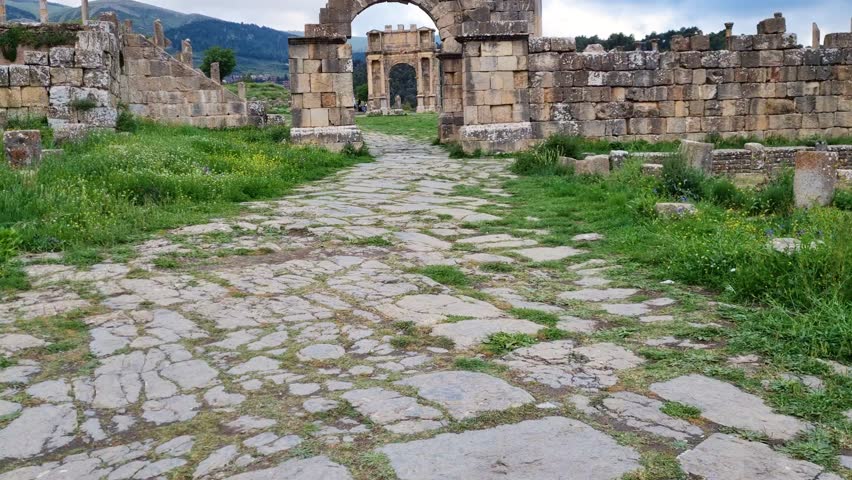 Revealing shot of arch gates and stone walls in the Roman ruins of Djemila in Algeria on a a cloudy day