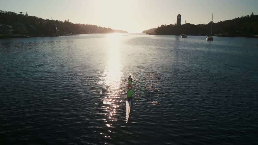 Drone Shot Four Rowers In Eight-Oar Boats Training At Sunrise. The Calm Ocean Waters And The Golden Sunrise Light Make For A Serene Scene Of Preparation For Their Upcoming Rowing Competition.