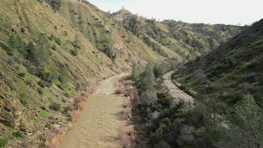 Golden hills and lush trees frame the flowing waters of Cache Creek in this overhead drone perspective.