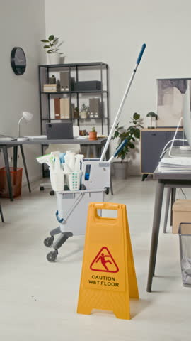 Vertical shot of caution wet floor sign and cleaning supplies with sprayers and detergents at empty modern office