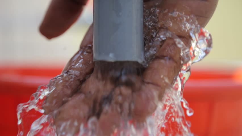 Young boy holds his hand under a stream of water coming from a tap in rural Africa