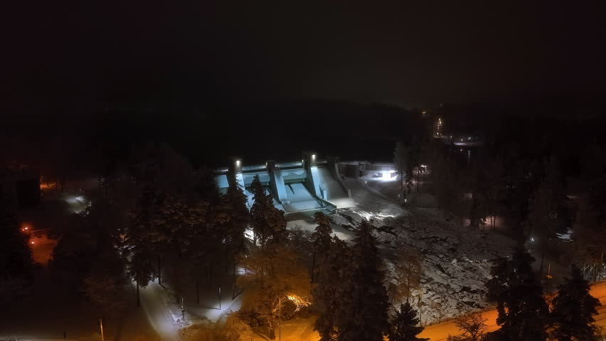 Panoramic drone shot orbiting the illuminated Imatra dam, winter night in Finland