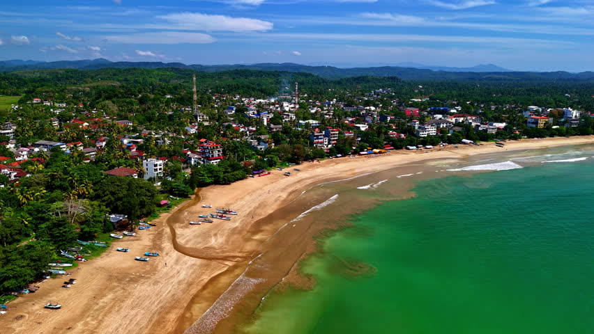 Drone aerial landscape of Weligama sandy beach bay ocean sea coastline with town village buildings resorts hotels and restaurants Sri Lanka travel tourism holidays