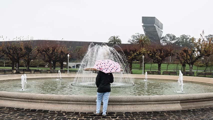 Young girl standing holding a pink heart pattern umbrella in front of a fountain in Golden Gate Park San Francisco California STATIC SHOT SLOW MOTION