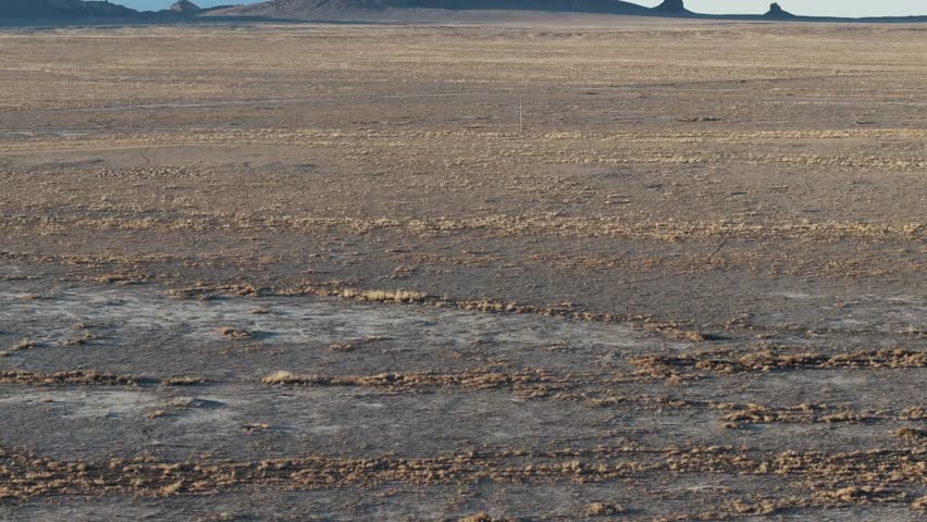 A low to the ground, slow-rising 70mm drone shot of the sacred “Ship Rock”, a massive, monolithic monadnock towering above the high-desert plain of the Navajo Nation, in New Mexico, United States.