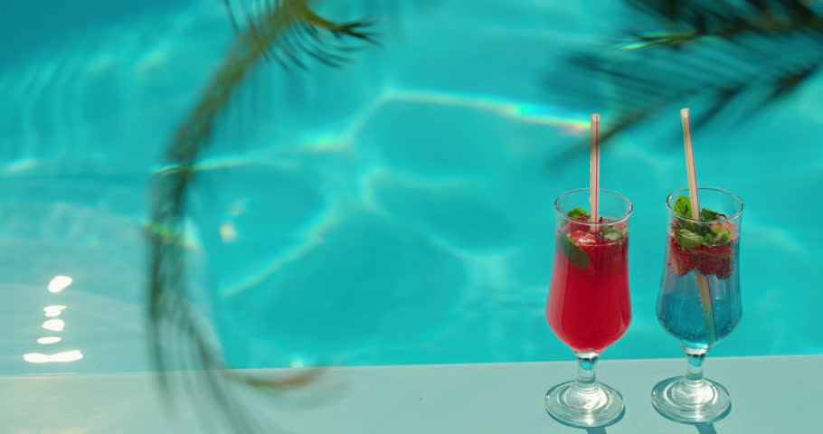 Two colorful cocktails with strawberries and mint by a turquoise pool, creating a refreshing and tropical summer vibe. High quality 4k footage