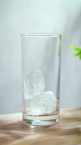 fresh sparkling orange juice drink pouring into a glass on sunny wooden kitchen tabletop and gray wall background, slow motion