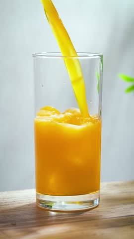 fresh sparkling orange juice drink pouring into a glass on sunny wooden kitchen tabletop and gray wall background, slow motion