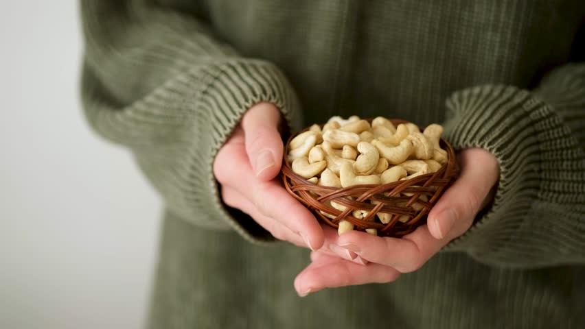 Eating cashew nuts. Bowl of cashew nuts in female hands