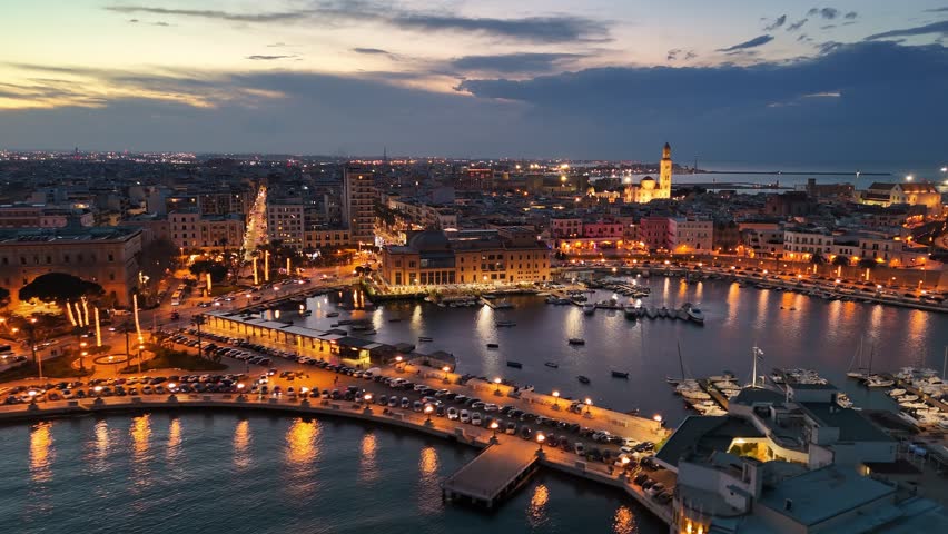 Aerial sunset view of Bari city lights and marina with yachts. Flight over the old town and the embankment of Bari, Puglia, Italy