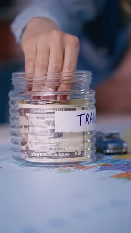 Female hand takes saved cash from a glass jar, budgeting for travel expenses