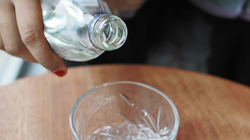 Pouring a refreshing glass of water into an icefilled glass on a table