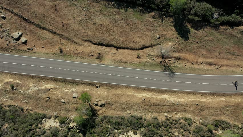Aerial view moving down the highway as a cyclist pedals past