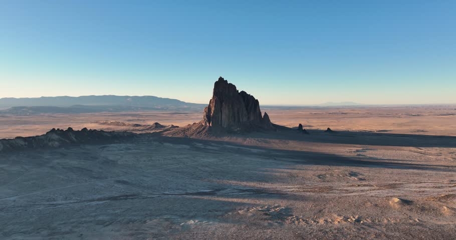 An unworldly high and far, wide-angle aerial shot of the sacred “Ship Rock”, a massive, monolithic monadnock, towering above the high desert plain of the Navajo Nation, in New Mexico, United States.