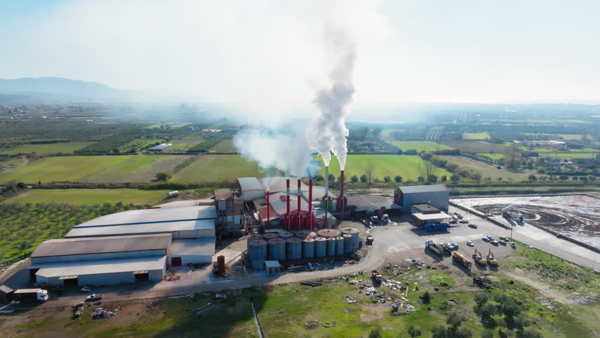 Slow panning drone of a rural factory emitting smoke out of its chimneys