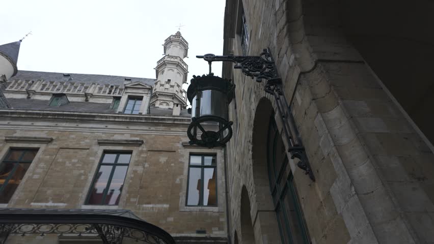 Low angle view of Brussels Town Hall courtyard featuring a hanging lamp, showcasing the gothic architecture and cloudy sky. Pan left