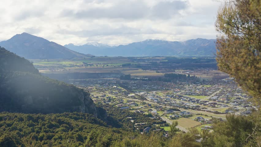 Beautiful natural landscape and Wanaka town in New Zealand during autumn. View from above over peaceful neighborhood and residential area surrounded by mountains and green trees. Mount Iron circuit
