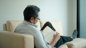 Back view of asian senior middle aged man enjoy spending weekend with reading a novel book while sitting on sofa at home, elderly man relaxing with book on comfy couch leisure retirement at home.
 - Powered by Shutterstock - Get 15% off with code: PIKWIZARD15