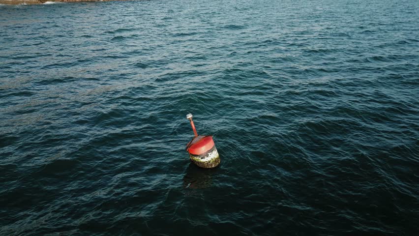 Aerial 4K slow-motion shot at 29.97fps over the Pacific Ocean. The drone remains stationary while the camera tilts down, centering on a red-topped buoy swaying with the blue waves.