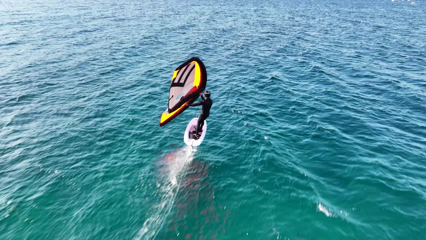 Aerial drone cinematic video of fit athlete practise hydro foil wing surfing in tropical exotic bay with emerald sea
