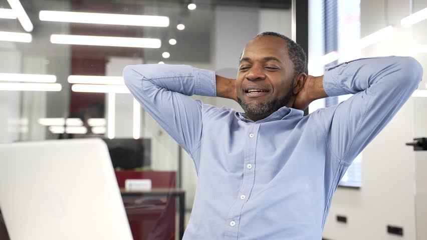 Happy african american businessman finished work on laptop while sitting at workplace in business office. Smiling satisfied black man puts his hands behind his head, leaning back in chair. Work done - Powered by Shutterstock - Get 15% off with code: PIKWIZARD15