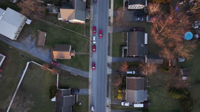 Red car on street of quiet American neighborhood during sunset time. Small suburb town in winter season. Roof of homes and houses. Aerial top down shot.