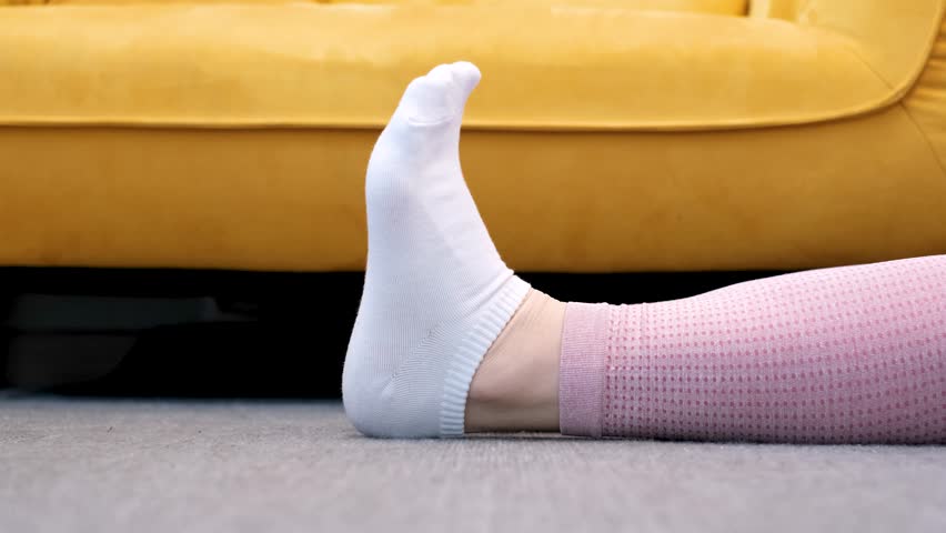 Female legs in socks bend and unbend feet against the background of yellow sofa.